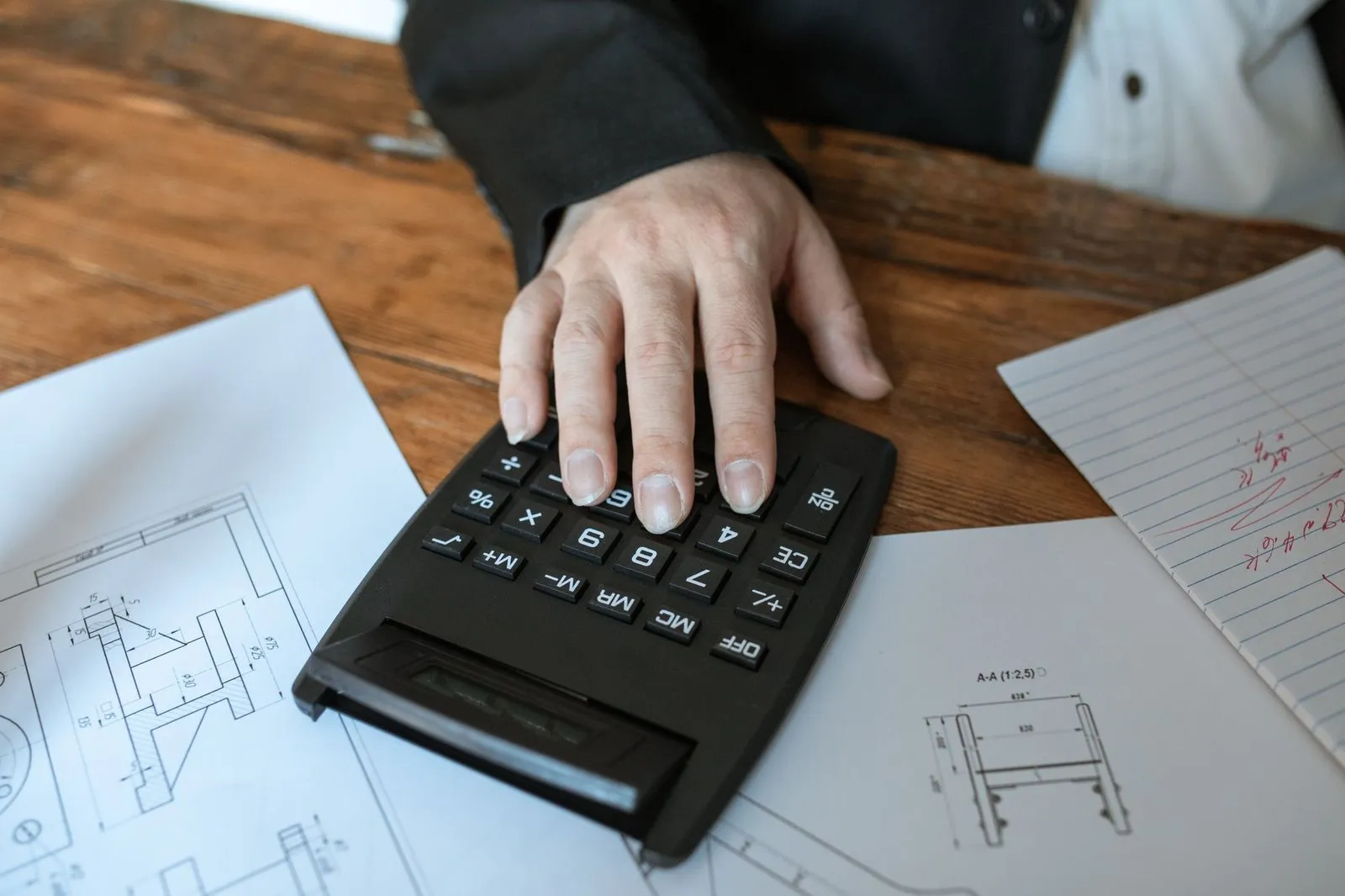 Main posée sur une calculatrice, plans et documents sur un bureau