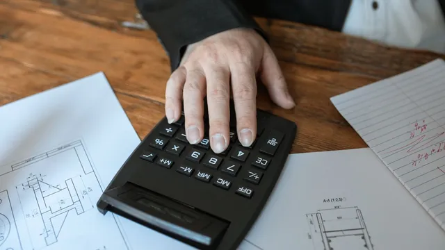 Main posée sur une calculatrice, plans et documents sur un bureau